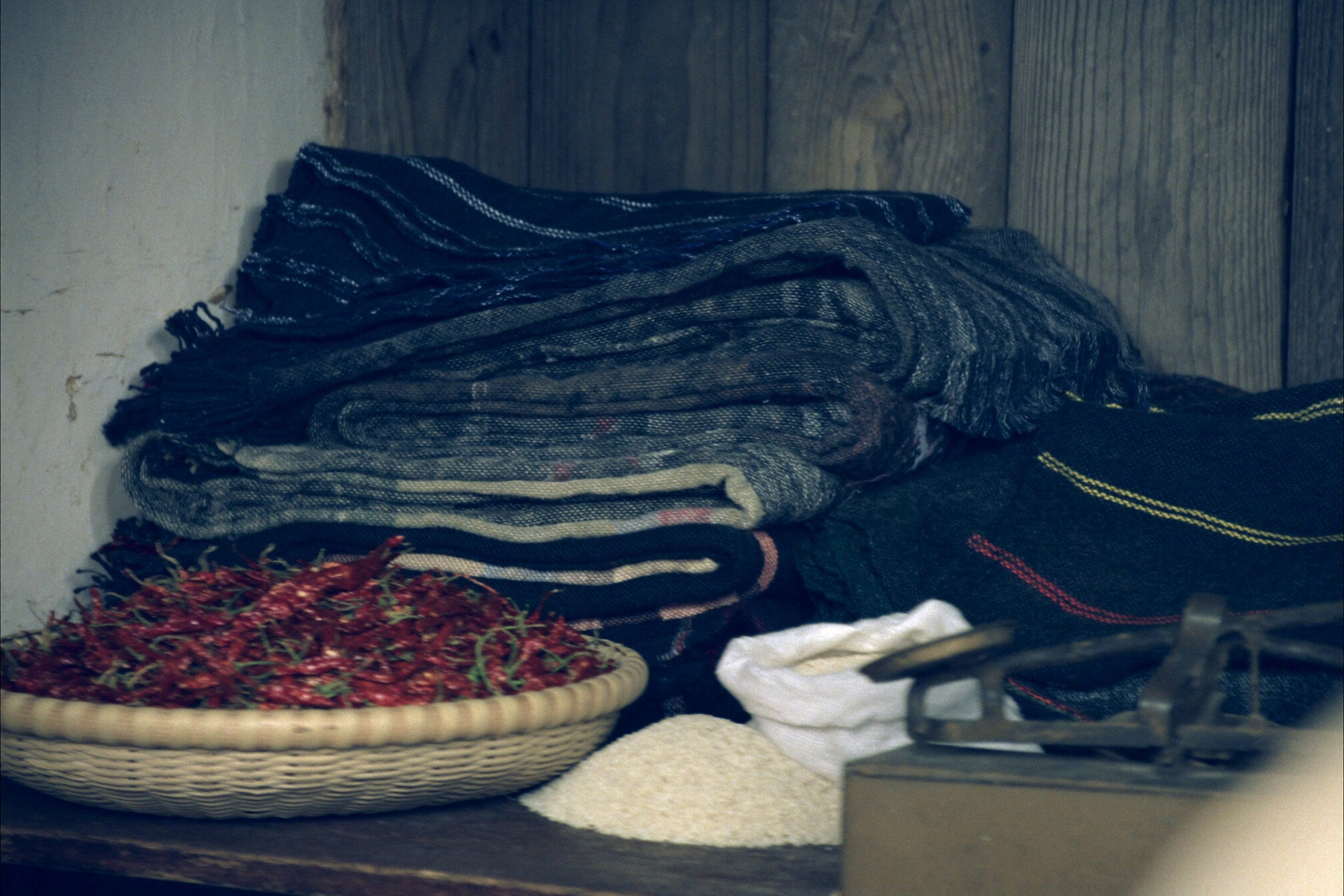 Folded handwoven textiles, a basket of dried chillies and a brass scale arranged on a wooden market table
