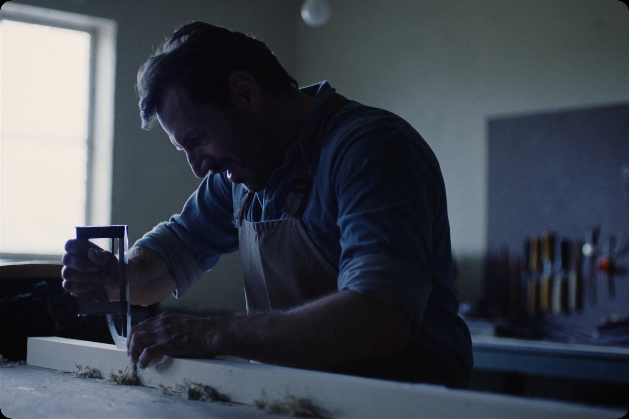 A tradesman in an apron measuring a length of timber against a steel square on a workbench