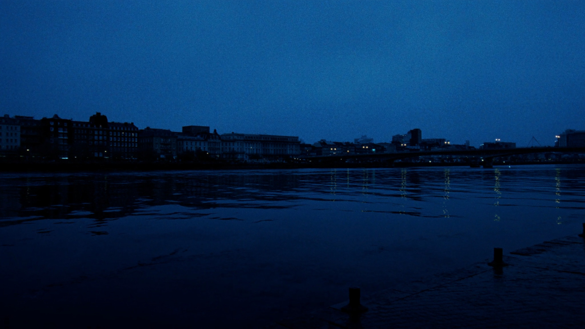 A city skyline across a broad river at blue hour, the water broken by small waves