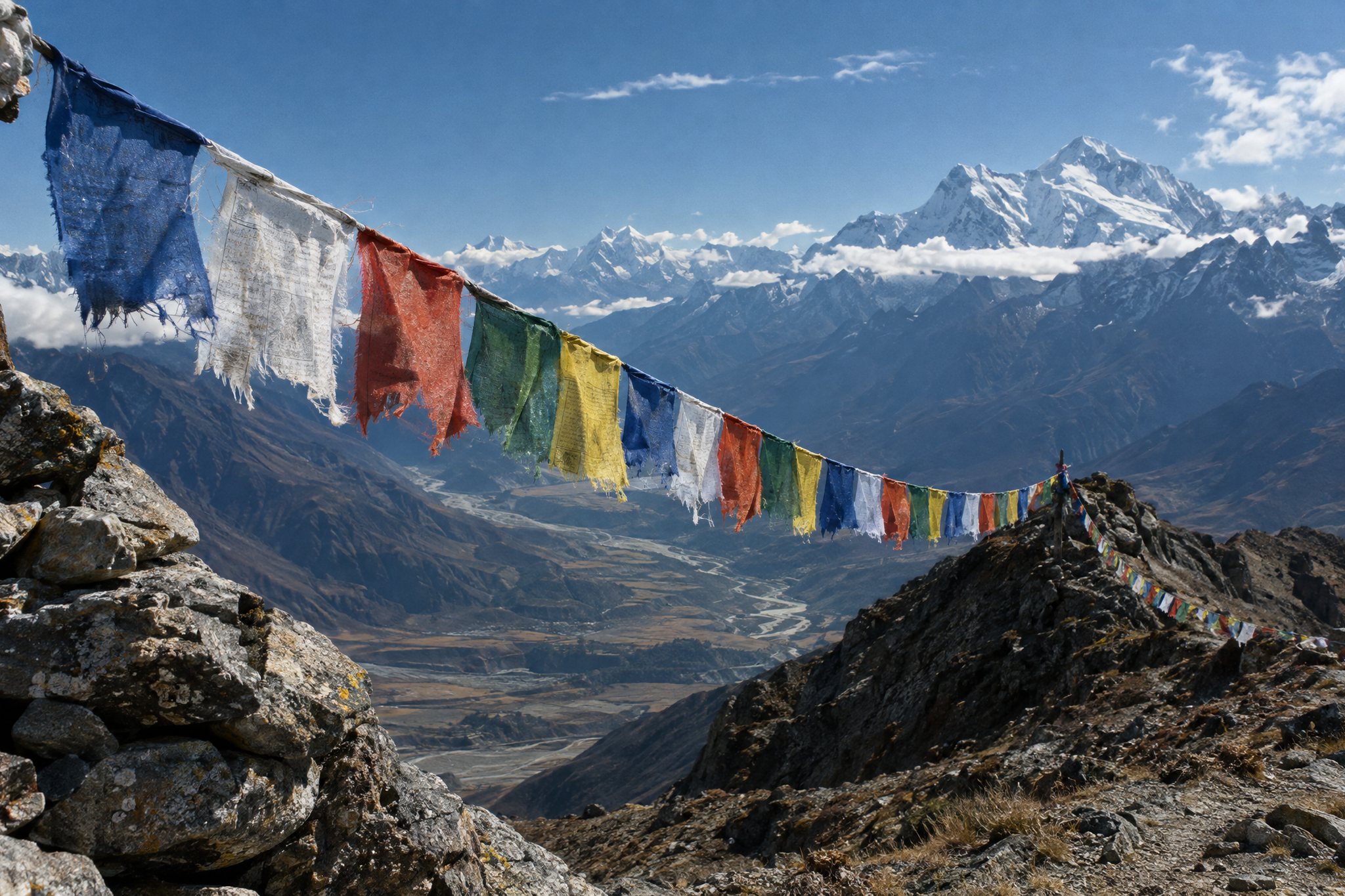 A line of five-colour prayer flags strung across a high ridge, the cloth frayed by the wind, a valley falling away below