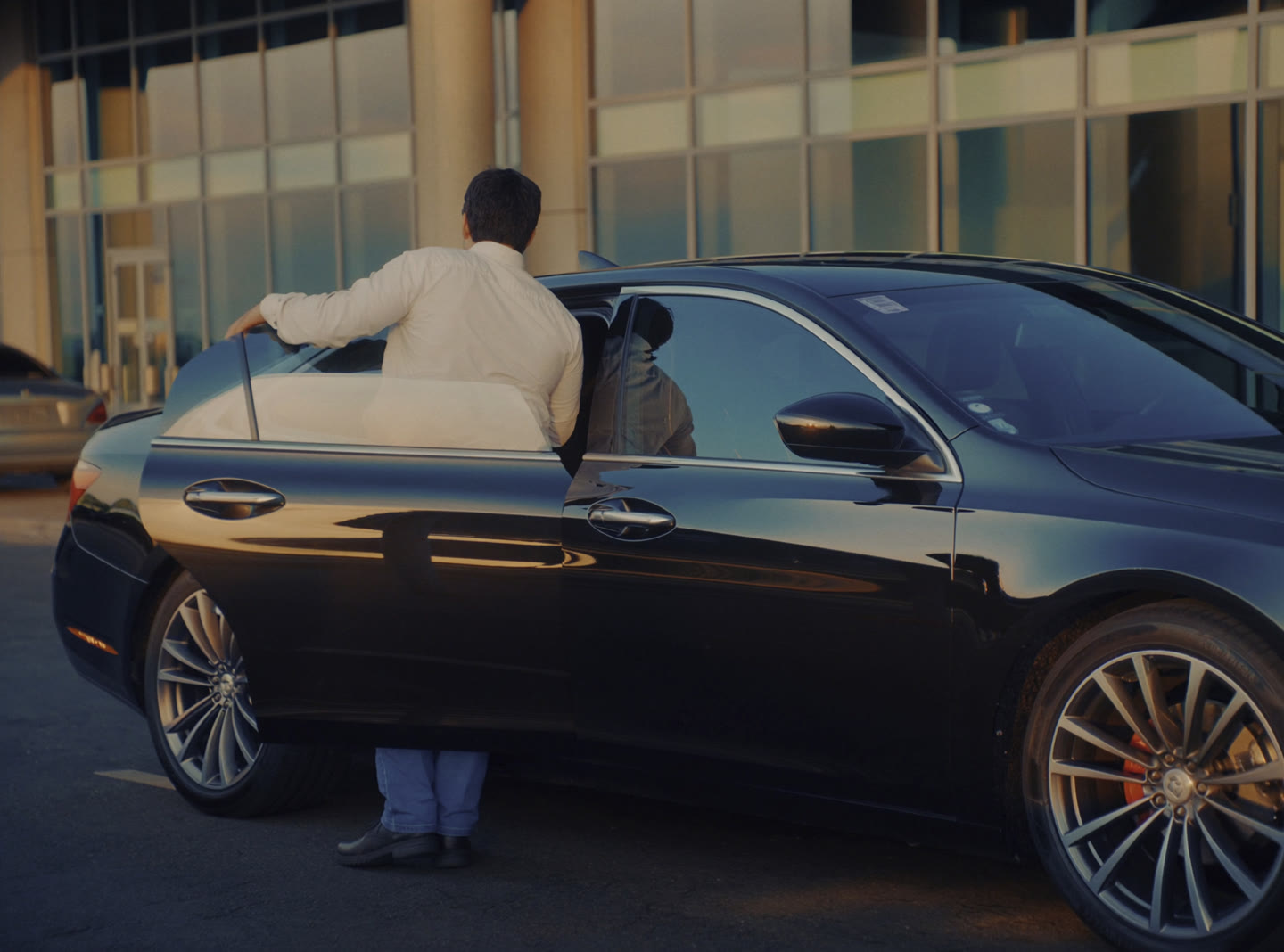 A clean dark sedan waiting at an airport terminal kerb with a driver beside the open rear door