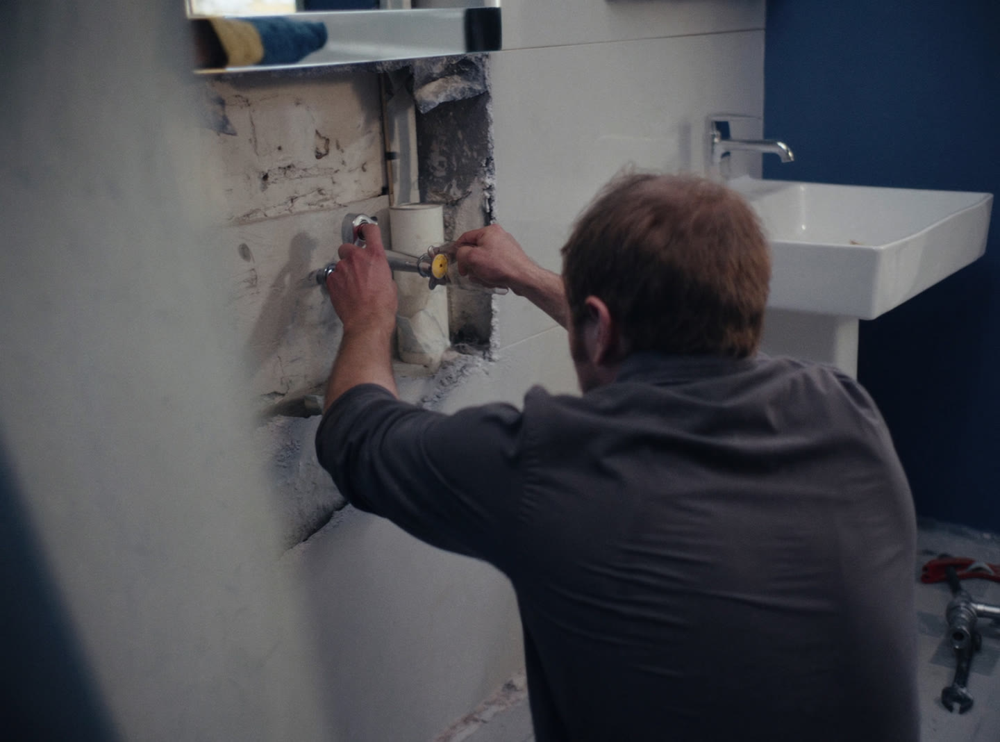A plumber fitting a new chrome mixer tap to a modern basin in a half-finished bathroom