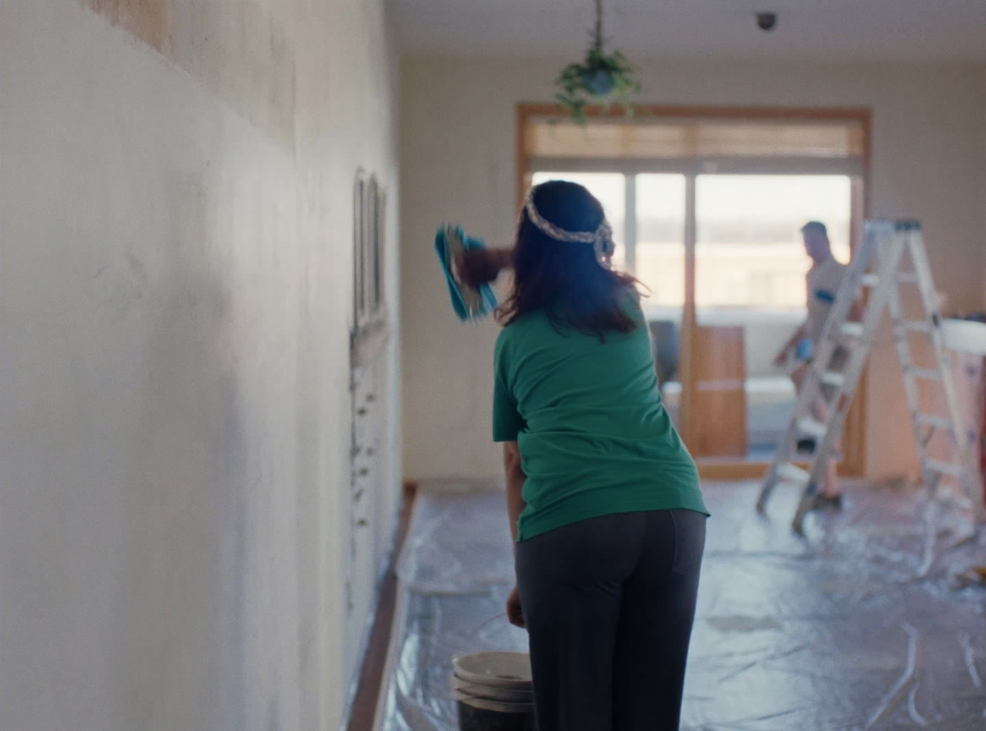 A cleaner wiping construction dust from a newly finished room, floor sheeting and a stepladder behind