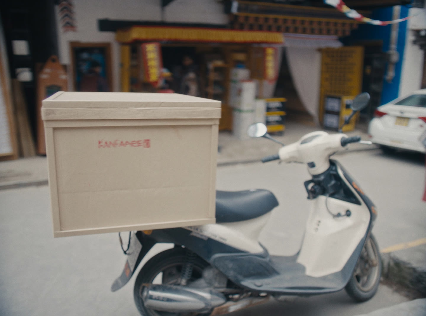 A step-through scooter fitted with a plain delivery box parked at the kerb of a quiet Bhutanese street