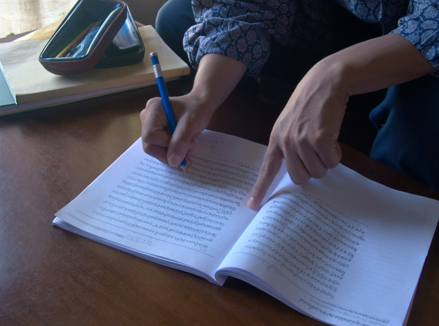 An adult learner writing Dzongkha script in an exercise book at a wooden table