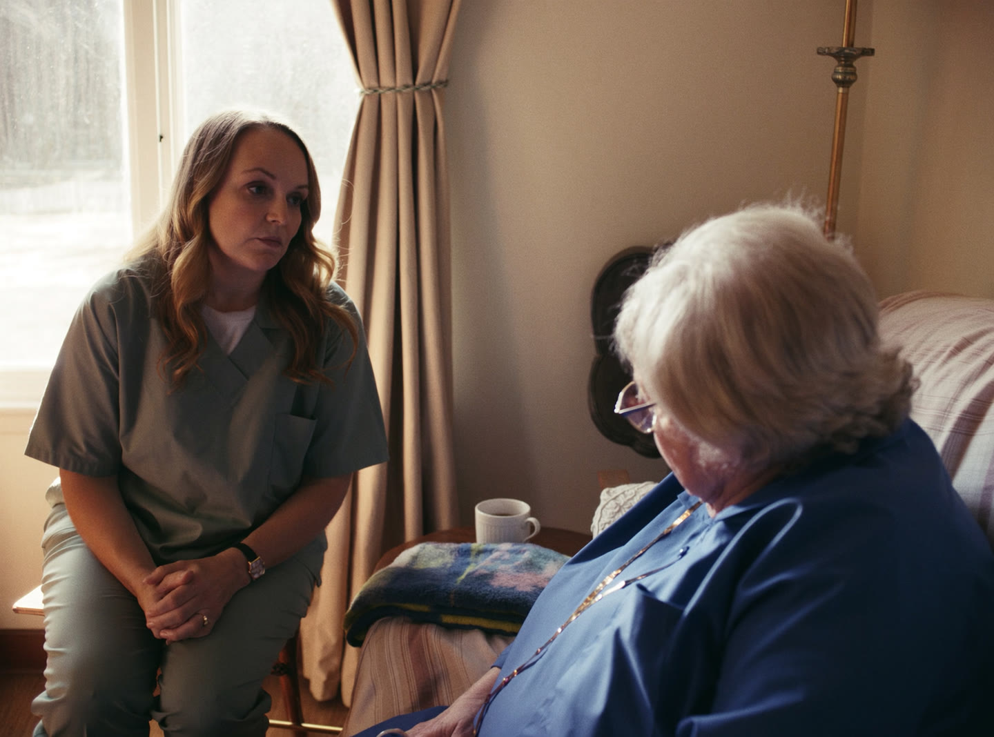 A care worker sitting beside an elderly woman in a bright living room