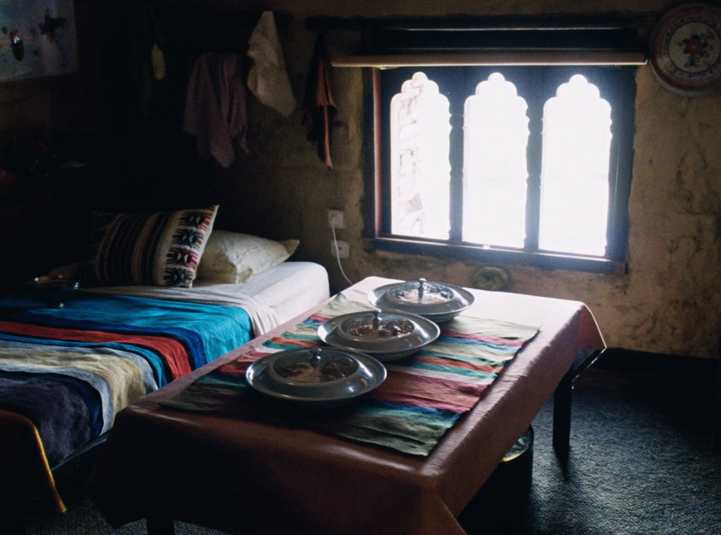 A Bhutanese farmhouse guest room, a made bed with a handwoven blanket and a low table set with three dishes
