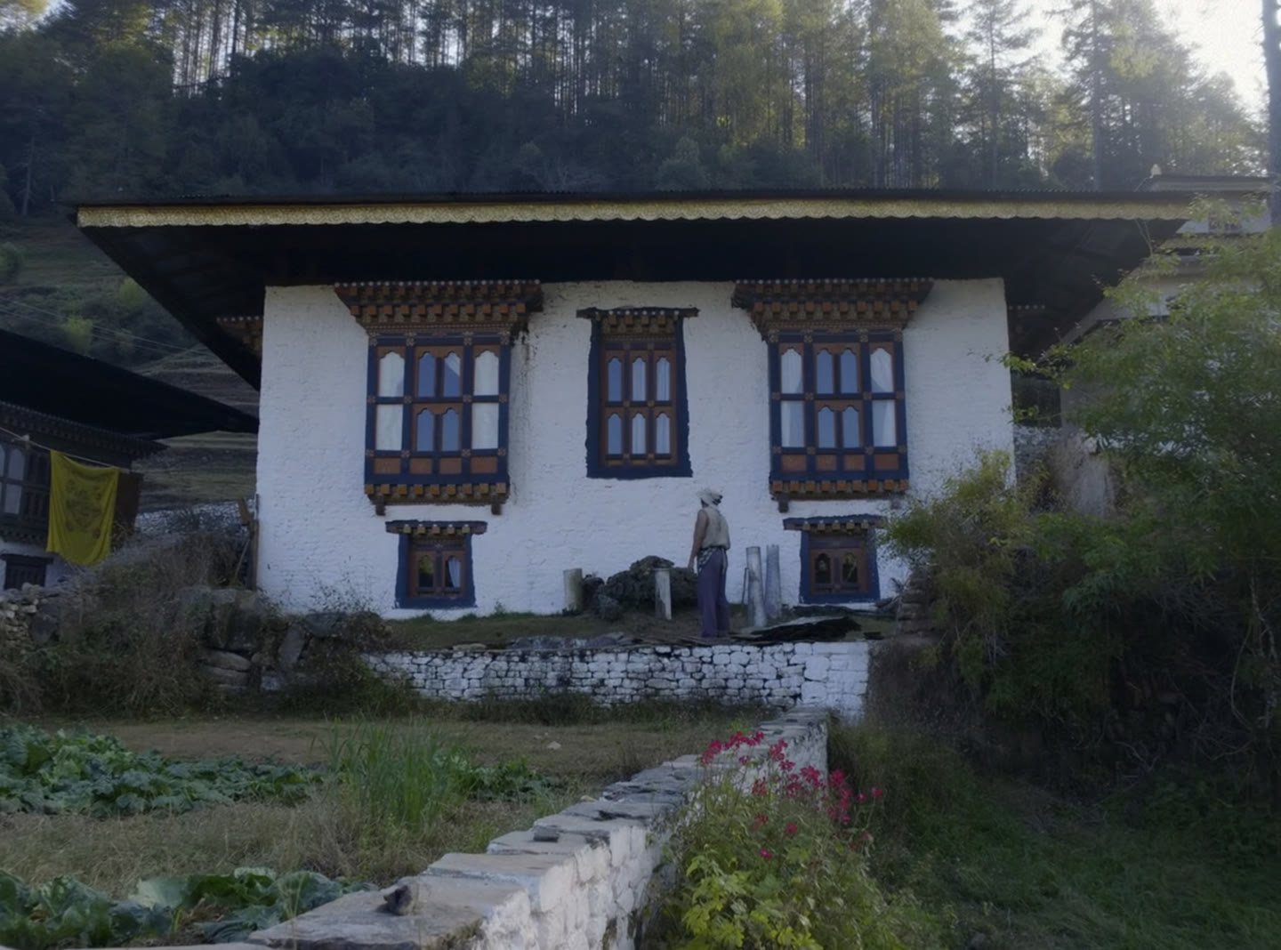 A three-bedroom Bhutanese house on a slope, whitewashed walls, a gilded roof edge and a walled kitchen garden