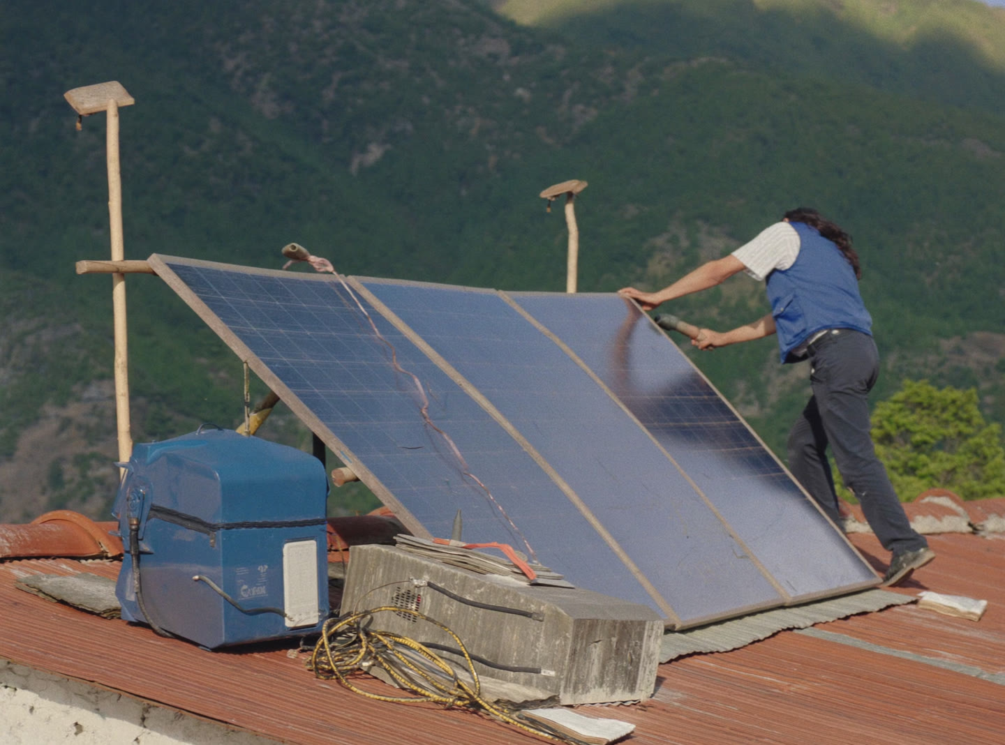 A technician mounting solar panels on a Bhutanese tiled roof with an inverter beside him