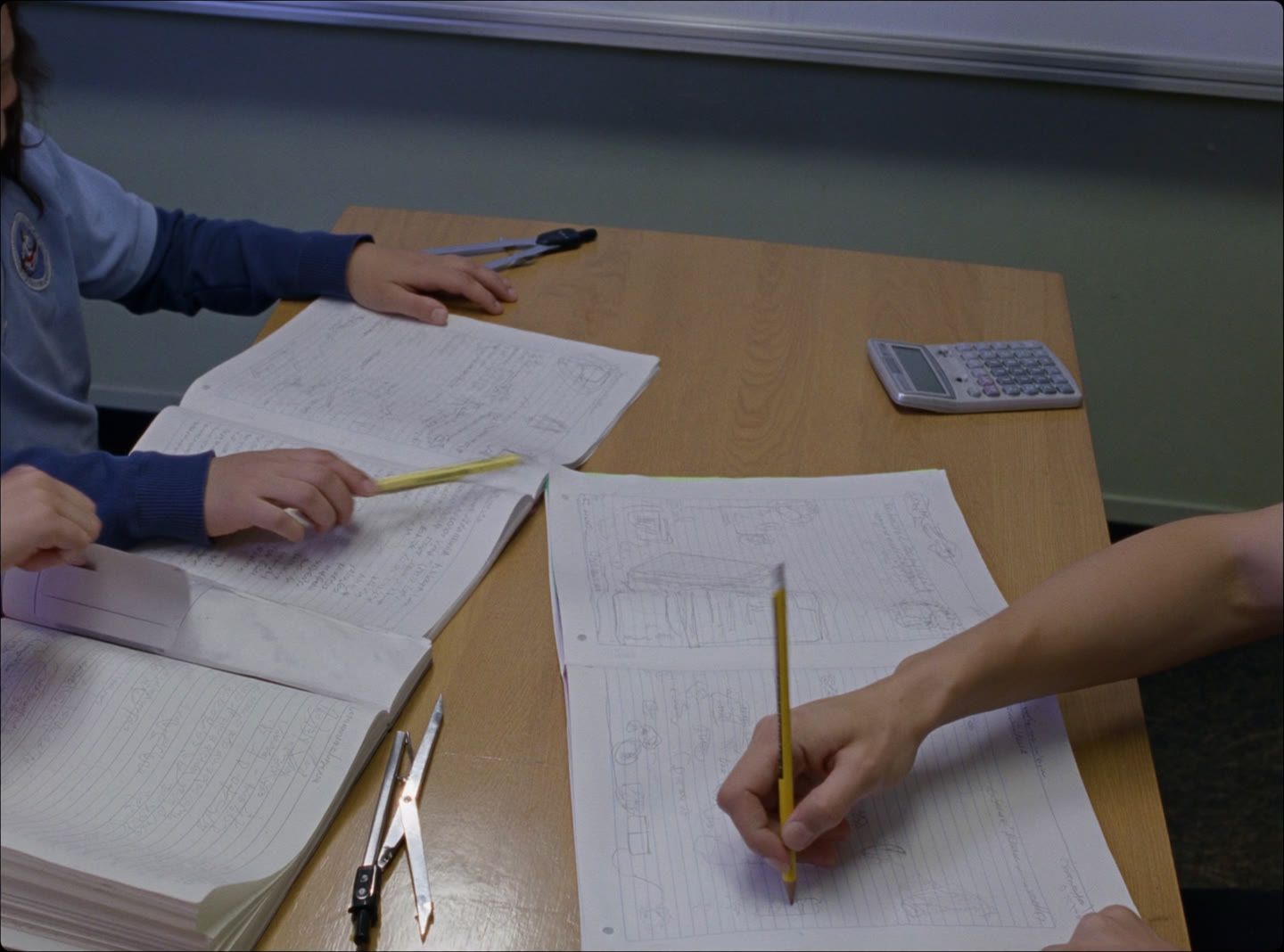 A small mathematics tuition group at a wooden table, open exercise books, a geometry set and a calculator