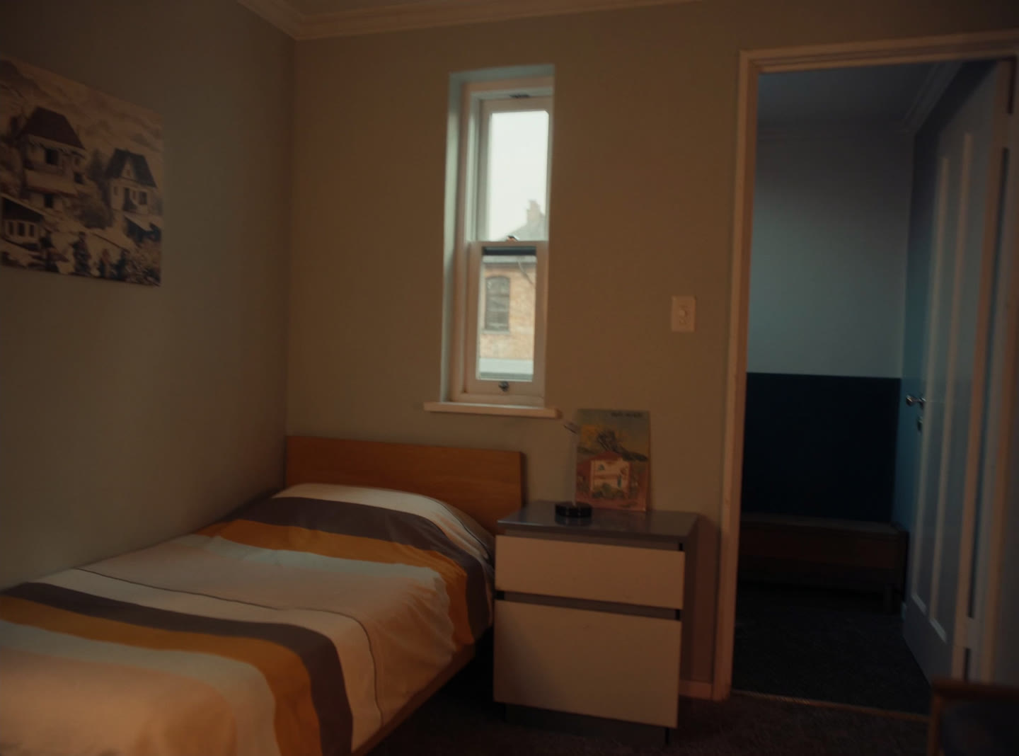 A furnished single bedroom in a shared suburban house, a bed with a striped cover and a small lamp