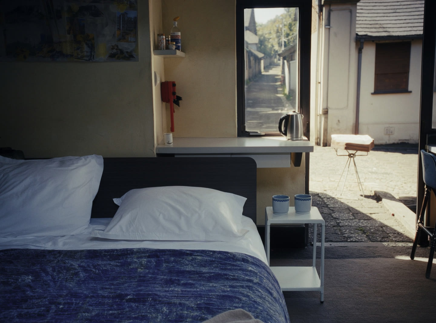 A compact studio flat with its own entrance, a made bed, a small kitchenette and a door open to a quiet lane