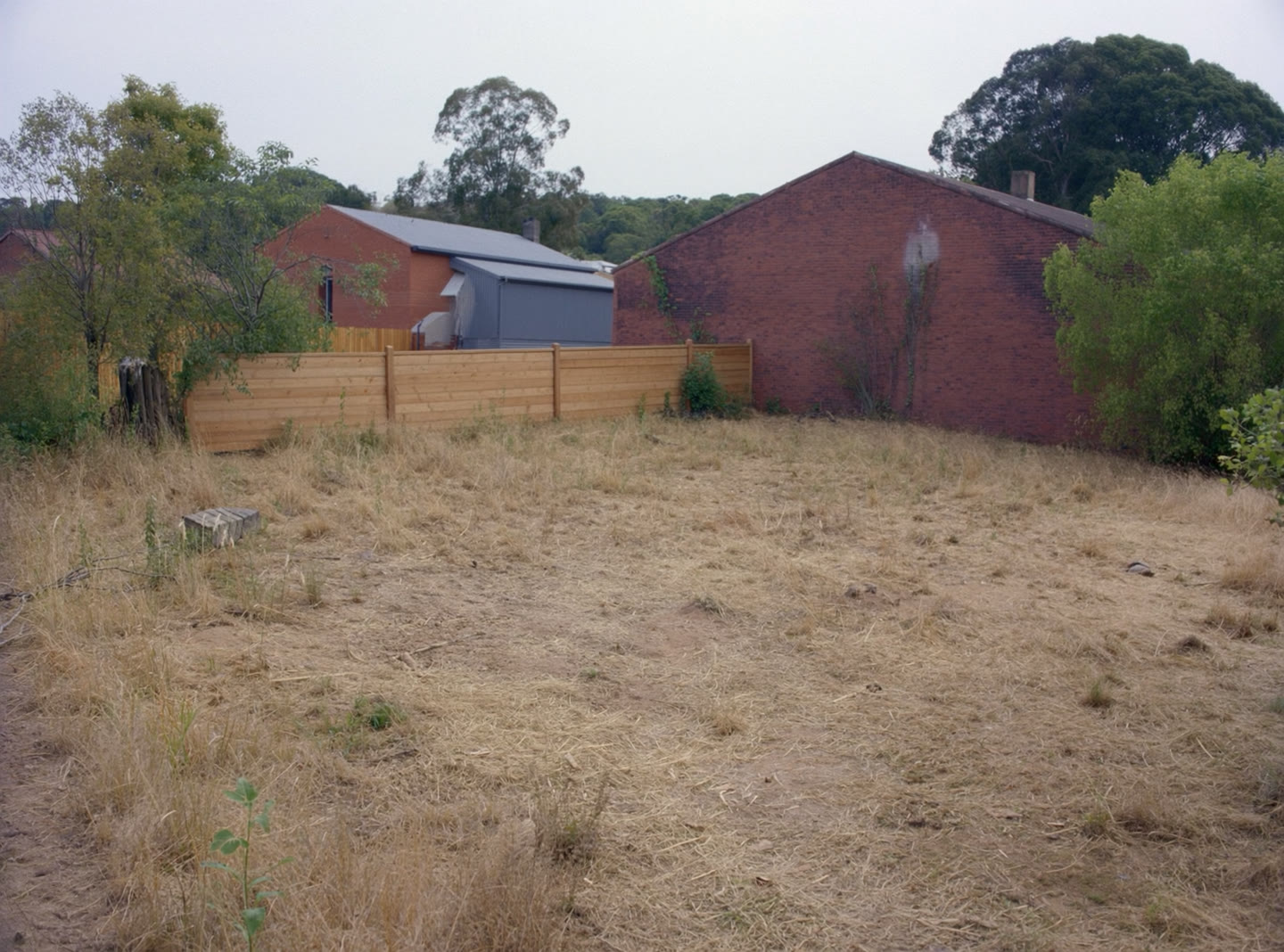 An empty residential building lot on an Australian suburban street with a low fence and brick houses