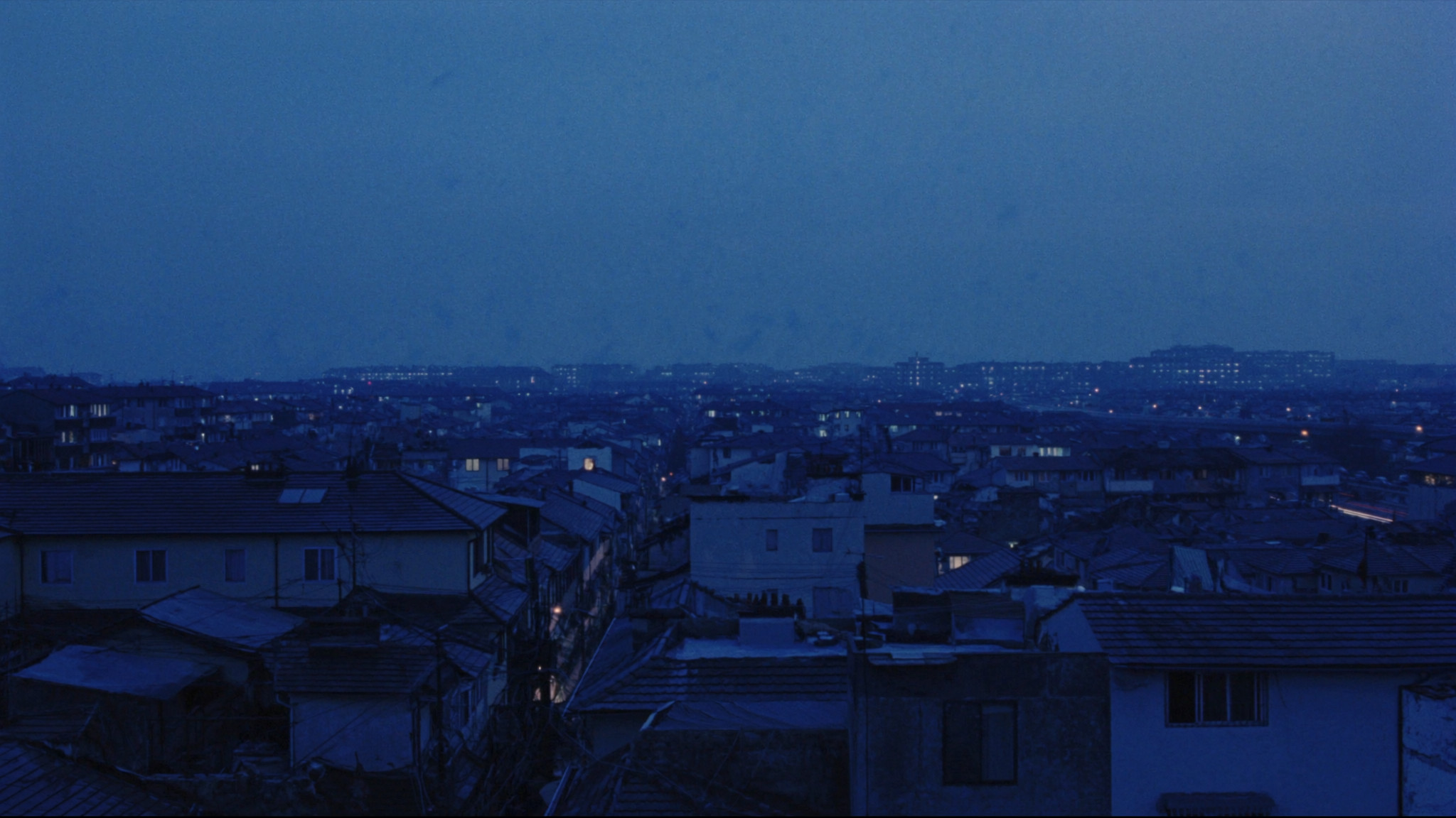 Rooftops of a dense low-rise city under a deep blue twilight sky